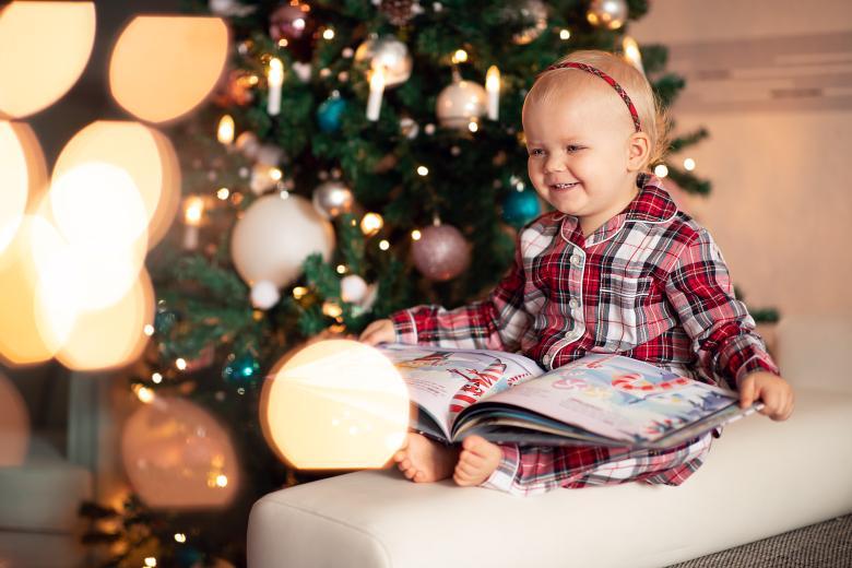 Little girl is smiling and reading from her personalized book about Christmas wishes.