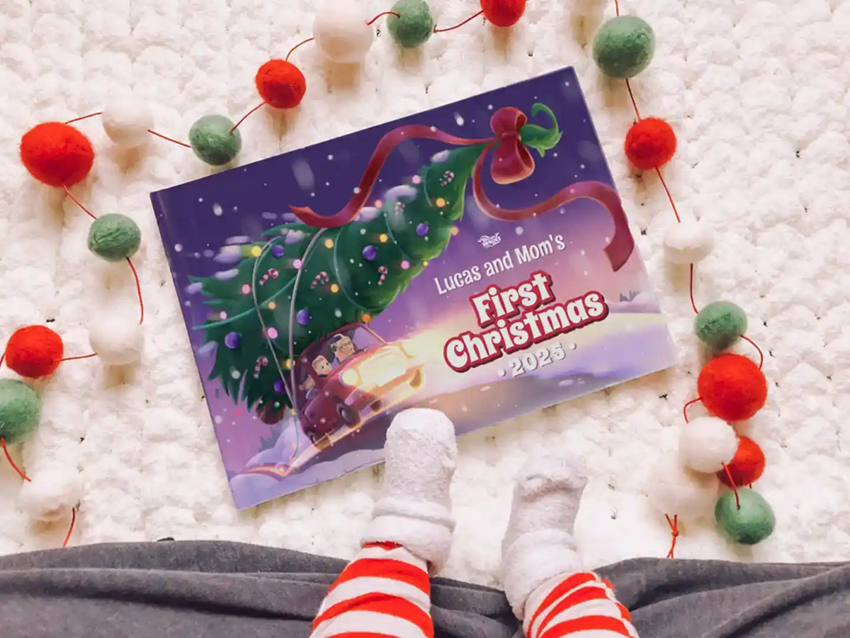 Personalized Christmas book titled “Lucas and Mom’s First Christmas 2025” lying next to baby’s feet and festive decorations.